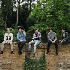 four young men sitting on top of a brick wall next to each other in front of trees