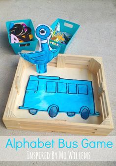 an alphabet bus game is displayed on the floor in front of a wooden tray with cardboard cutouts