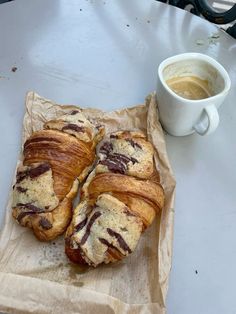 two croissants sitting on top of a piece of wax paper next to a cup of coffee