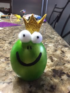 a green apple with two googly eyes and a gold crown on top