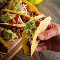 a hand holding a tortilla filled with meat, cheese and guacamole