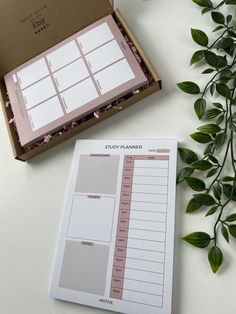 an open planner sitting on top of a table next to a plant