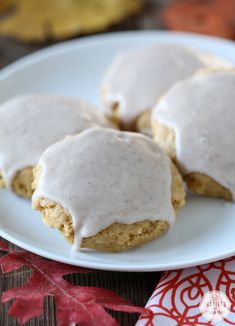 three frosted cookies on a white plate with red leaves in the backgroud