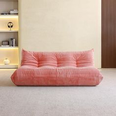 a pink futon sofa sitting on top of a carpeted floor next to a book shelf