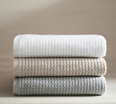 three white towels stacked on top of each other in front of a beige wall and floor