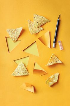 some tortilla chips and a pen on a yellow background with orange paper cut into triangles