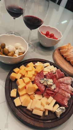 cheese, meats and olives are arranged on a platter next to two glasses of wine