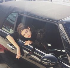 a woman sitting in the drivers seat of a car next to a black dog on her lap