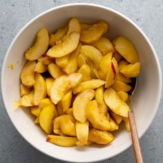 a white bowl filled with sliced peaches next to a wooden spoon on a gray surface