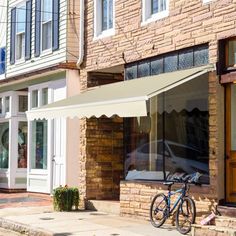 a bicycle parked on the side of a street next to a brick building with an awning over it