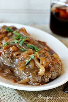 a white plate topped with meat covered in gravy and onions next to a fork