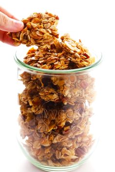 a hand is picking up some granola from a glass bowl on a white background