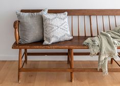 a wooden bench with two pillows on it and a blanket draped over the seat next to it