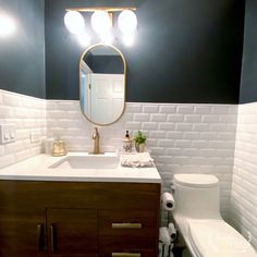 a white toilet sitting next to a sink in a bathroom under a mirror and lights