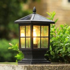 a light that is sitting on top of a cement block in front of some bushes