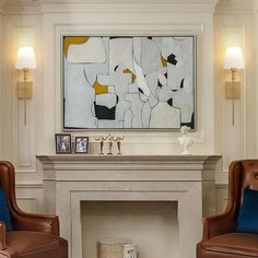 two brown chairs sitting in front of a fireplace with a painting on the wall behind them