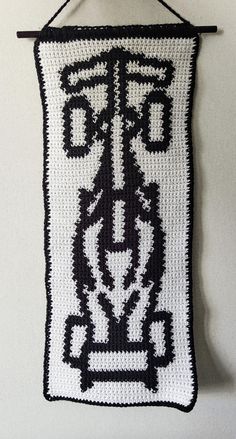 a black and white crocheted wall hanging on the wall with an iron hook