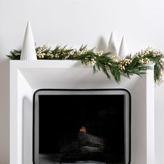 a white fireplace decorated with greenery and cones