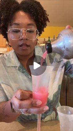 a woman pouring something into a glass with a pink substance in it and another person behind her