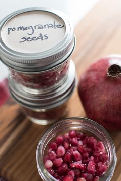 two jars filled with pomegranate seeds sitting on top of a wooden table