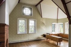 an empty room with wooden floors and two windows in the wall, along with a bench