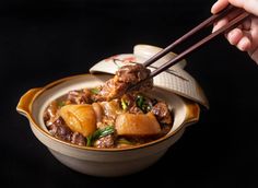 a person holding chopsticks over a bowl of food with meat and vegetables in it