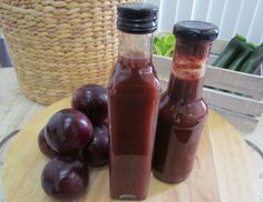 two bottles of plum jam sitting on top of a cutting board next to some plums