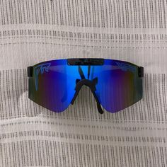 a pair of sunglasses laying on top of a white and gray striped cloth with blue mirrored lenses