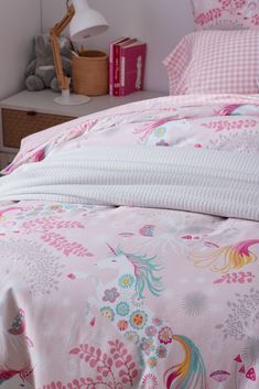 a pink bed with unicorns and flowers on the comforter is next to a night stand