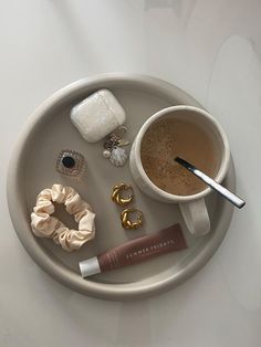 a white plate topped with a cup of coffee next to jewelry and a pair of scissors