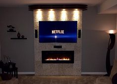 a living room with a large television mounted on the wall and a fire place in front of it