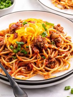 two plates of spaghetti with meat, cheese and green onions next to some peas on the side