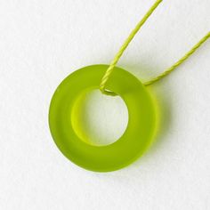 a green necklace with a yellow string on white paper and an orange cord hanging from it