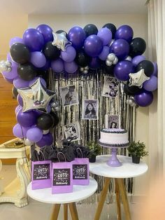 a table topped with purple and black balloons next to a cake on top of a table