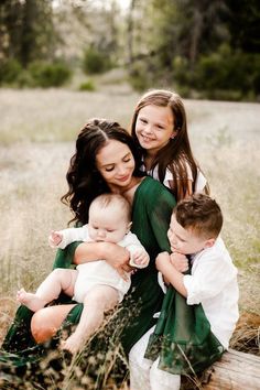 a mother and her two children are sitting on a bench in the grass with their arms around each other