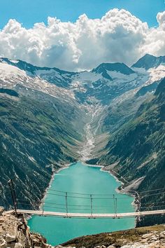 a bridge that is over looking a lake in the middle of mountains with snow on them