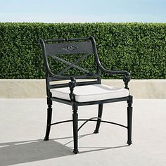 a black and white chair sitting on top of a cement floor next to a hedge