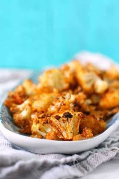 a white bowl filled with cooked cauliflower on top of a tablecloth next to a blue wall