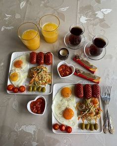 three plates with eggs, sausages, tomatoes and olives next to glasses of orange juice