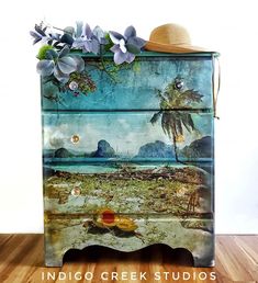 an old dresser has been painted with tropical scenes and flowers on the top, along with a straw hat