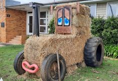 a tractor made out of hay sitting in front of a house with blue eyes on it