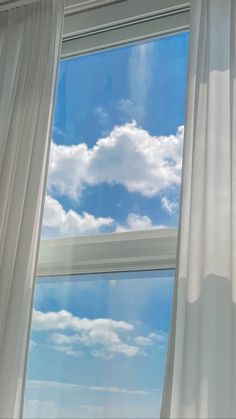 there is a window with white curtains and blue sky in the background