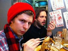 two men sitting at a table with food and chopsticks in front of them