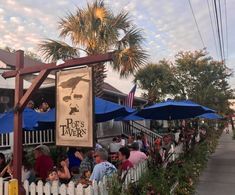 many people are sitting at tables under blue umbrellas on the side of the road