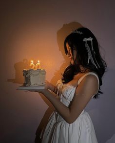 a woman in a white dress holding a cake with two candles on top of it