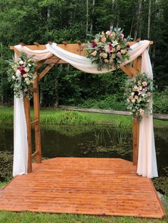 a wooden gazebo decorated with flowers and white drapes for an outdoor wedding ceremony