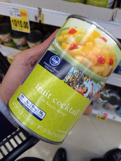 a person holding up a can of fruit cocktail in a grocery store's aisle