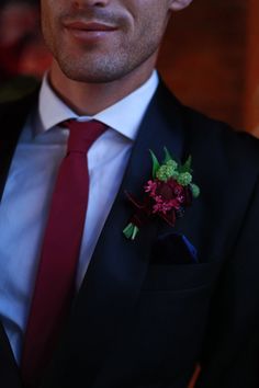 a man in a suit with a red tie and flower boutonniere on his lapel