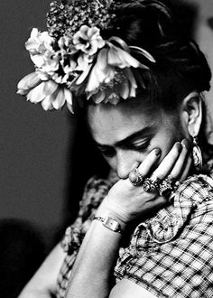 a black and white photo of a woman with flowers in her hair holding her hands to her face