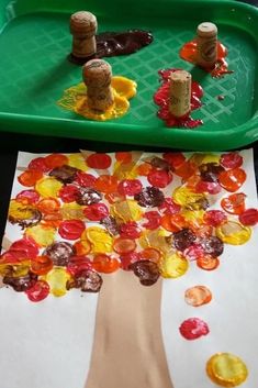 a child's hand is painting a tree on paper with buttons and corks